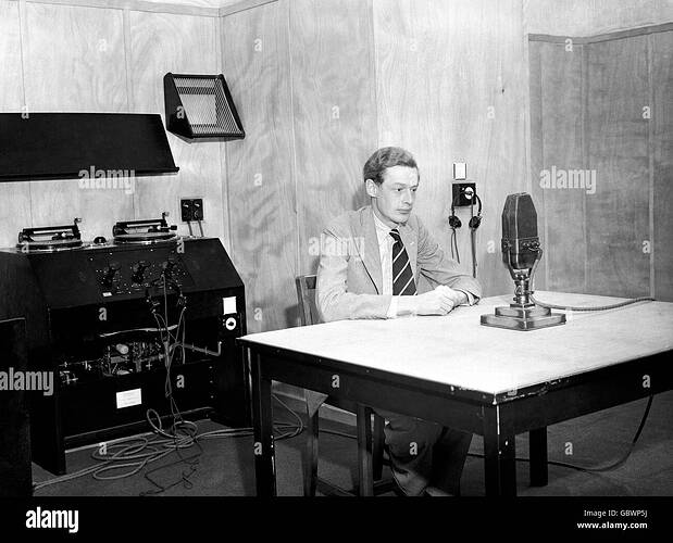 olympische-spiele-bbc-broadcasting-center-fur-die-olympischen-spiele-1948-in-london-palace-of-arts-wembley-ansager-in-einem-studio-mit-einem-mikrofon-vor-ihm-und-einem-grammophon-das-im-hintergrund-gerate-reproduziert